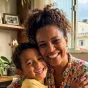 Mãe abraçando o filho enquanto os dois sorriem juntos no sofa.